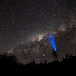 photo of a person in a nighttime starry night scene, shining a flashlight beam towards the sky
