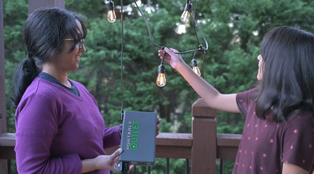 Photograph of two young women powering outdoor string lights with the Portable Outlet CPAP Battery